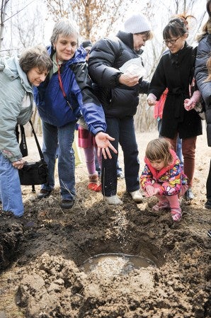 Nature Center employee  Jill DeMoss, blue coat, spreads ashes of  Red during a tree planting ceremony. 