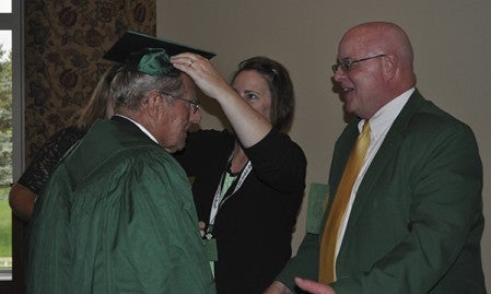 Pacelli Catholic Schools officials help Paul Rysavy don a graduation cap and gown to receive his high school diploma Saturday, during an alumni banquet celebrating the school's 100th anniversary.