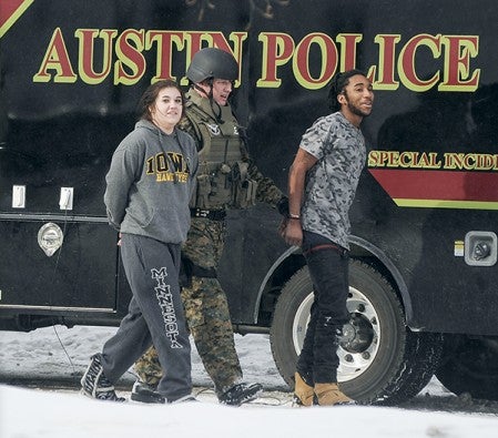 A member of the Austin Special Incident Response Team leads a 17-year-old male and 15-year-old female to a waiting squad car after being arrested.
