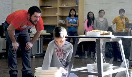 Science teacher Clint Phillips, left, watches as sixth-grader Isaac Aguilar adds weight to a bridge he made as part of a challenge at the first annual STEAM Expo at I.J. Holton Intermediate School Wednesday. Trey Mewes/trey.mewes@austindailyherald.com