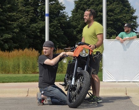 Charlie Smithson, left, and Taylor Bamber tune up the Driven By Bacon motorcycle in front of Hormel Foods Corp.’s North Corporate Office Monday. Smithson, a mechanical engineer, and Bamber designed the motorcycle to run on refined bacon grease. Trey Mewes/trey.mewes@ austindailyherald.com