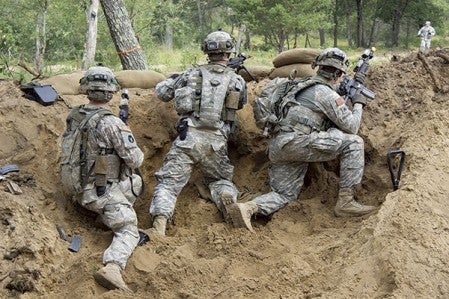 Three soldiers watch from behind a berm during a defensive exercise. 
