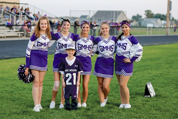 Grand Meadow brought back football cheerleaders for the first time in five years thie fall. The team, pictured with Carter Simonson, an honorary captain at last week's game,  includes: (left to right): Faith Gehling, Haley Kestner, Katarina Bain, Autumn Speer, and Nathalia Cortes. Simonson was diagnosed with T Cell Leukemia this past December. -- Photo Provided by Rhonda Besel
