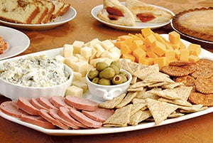 A tray of cheese, crackers and dips on a table with baked party foods