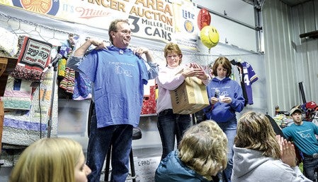 Lyle Area Cancer Auction co-chair Larry Ricke displays a shirt given him by Teresa Slowinski, right, after it was announced the auction hit the $2 million mark. Joing them is Cindy Ziegler. Eric Johnson/photodesk@austindailyherald.com