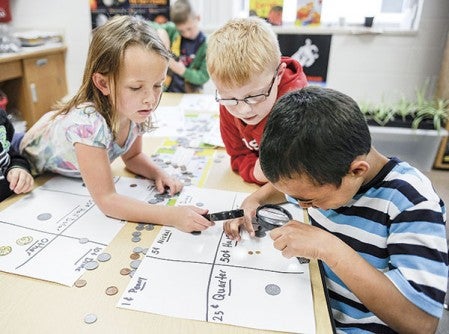 Moyra Voigt, from left, Leighton Ruhter-Wencl and JayVon Towers investigate coins from South America in Jason Denzer’s class at Woodson Kindergarten Center. Eric Johnson/photodesk@austindailyherald.com