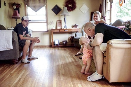Ruroden reaches down to kiss his grandaughter Adalyn at the family’s home Thursday afternoon as he sits with his daughter Brandi and future son-in-law Taylor Bordelon. 