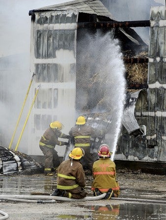 A pair of firefighters rip pieces of tin from the side of a shed as another pair puts water on the burning straw inside the shed on a farm south of Rose Creek Tuesday afternoon. Both Rose Creek and Adams fire departments responded. Eric Johnson/photodesk@austidnailyherald.com