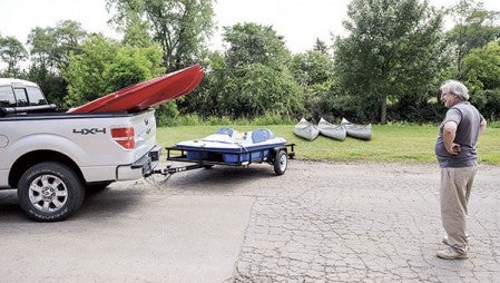 Brian Pirmantgen waits as a truck loaded with kayaks and a paddleboat are backed into position to be unloaded next to the Cedar River.  Eric Johnson/photodesk@austindailyherald.com