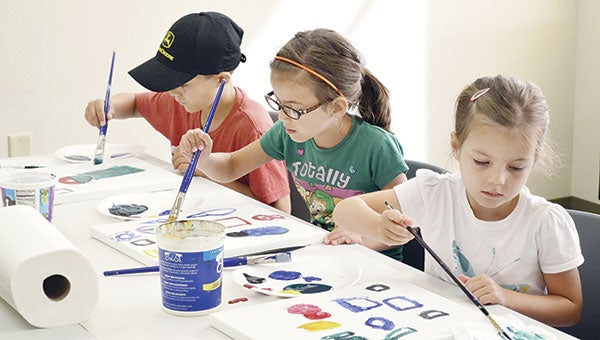 Siblings Easton, 8, Emma, 7, and Isabella Schmitz, 5, paint the shapes they see on a table in the middle of the room at the Mower County Libraries Traveling Art Studio at the Austin Library Monday. Photos by Jenae Hackensmith/jenae.hackensmith@austindailyherald.com