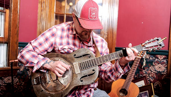 Teacher by day, musician/artist by night, Jesse Smith picks at his custom steel guitar from his Austin Home. Eric Johnson/photodesk@austindailyherald.com