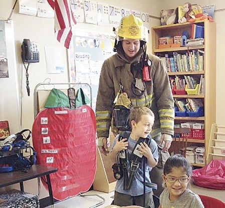 Firefighter Brandon Slowinski of the Lyle Fire Department watches Thursday as kindgartener Dayne Ransom tries on some equipment. Also pictured is kindgartener Araceli Melendrez, right. Firefighters visited the school as part of Fire Prevention week. -- Photo provided by Melanie Jiskra