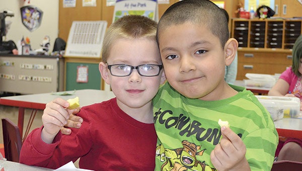 Gavin Wiedemann (left) and Alejandro Huerta Maldanado hold up their apple slices during snack time Tuesday morning. The apples are part of a healthy snack program that Woodson received a grant for last summer. Jenae Hackensmith/jenae.hackensmith@austindailyherald.com