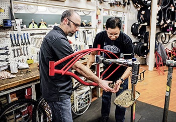 Gareth Hataye, right, and John Burkhart work together to start assembling one of the red bikes for the Red Bike Program Saturday morning at Rydjor Bike. 