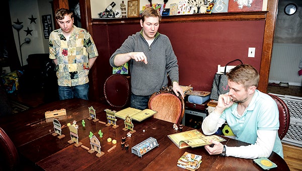 Michael Jordal, center, explains the rules to a new game called “Flick ‘Em Up!” With friends Jesse Qualey, right, and Gary Meyer, left, during a weekly game night at Jordal’s home. Jordal will host the first ever Austi-Con this weekend.  -- Herald file photo