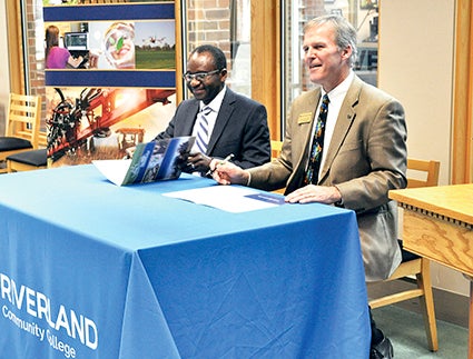 Riverland Community College president, Dr. Adenuga Atewologun, right, and Brad Schloesser, director of the Southern Minnesota Center of Agriculture, sign an agreement that would see Riverland joining the collaborative group that focuses on sustaining an ag workforce.