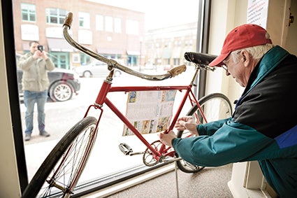 Steve Kime attaches a flyer for the Red Bike program to one of the red bikes displayed in a storefront window on Main Street. Austin Living. Herald file photo