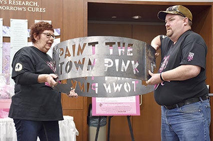 Paint the Town Pink committee member Judy Enright and her Hoot & Ole’s co-owner Jeremy Olson hold up an auction item. 