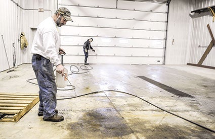 Paul Halbach puts down a cleaner to losen up grease on the floor of the Lyle Municipal Department’s building in preparation for the upcoming Lyle Area Cancer Auction this weekend. Eric Johnson/photodesk@austindailyherald.com