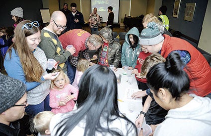 Kids and adults gather around a table at the Austin Public Library as they take part in an experiment. 