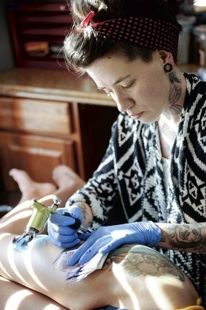 Misty Chastain tattoo’s sunflowers on her leg of Andrea Nolan at Corpus Opus Tattoo. Eric Johnson/photodesk@austindailyherald.com